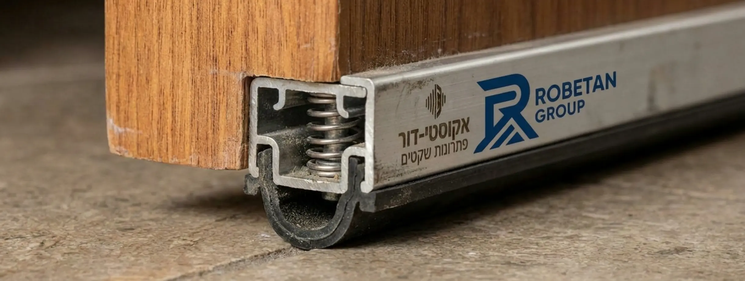 תקריב של סף אקוסטי אקטיבי המותקן בתחתית דלת עץ ויורד כלפי הרצפה בעת סגירת הדלת כדי לאטום את המרווח